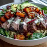 A generous drizzle of lime cilantro dressing brightens the hearty butternut squash steak bowls, garnished with crisp red onion.