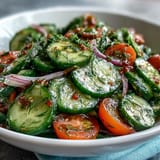 Sliced cucumbers in a tangy vinegar dressing make up the Refreshing Crunchy Cucumber Salad, garnished with fresh herbs.
