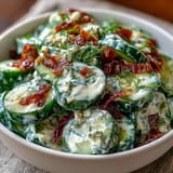 Creamy cucumber salad with dill and Greek yogurt in a white bowl, garnished with fresh dill sprigs and black pepper.