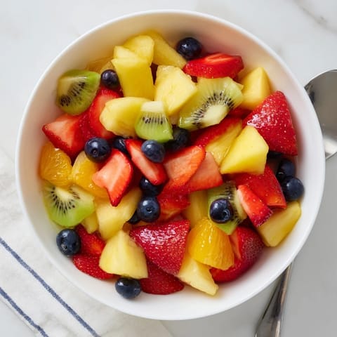 A vibrant bowl of Fruit Salad features fresh strawberries, kiwi, and blueberries glistening with citrus syrup.