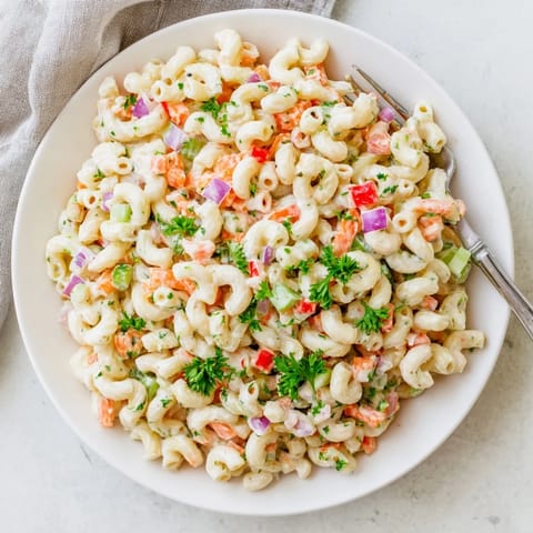 Classic Macaroni Salad served in a clear glass bowl on a picnic blanket, showcasing its creamy dressing and colorful crunchy vegetables.