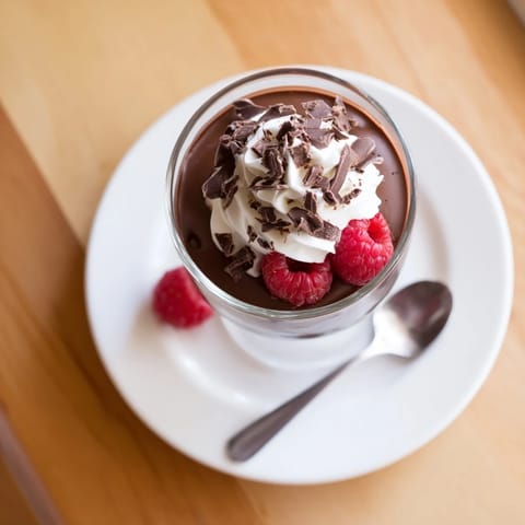 Creamy chocolate pudding in a glass topped with chocolate shavings and fresh raspberries.