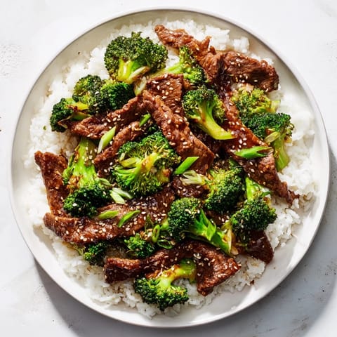 Steaming beef and broccoli stir-fry in a savory sauce over fluffy white rice in a bowl.