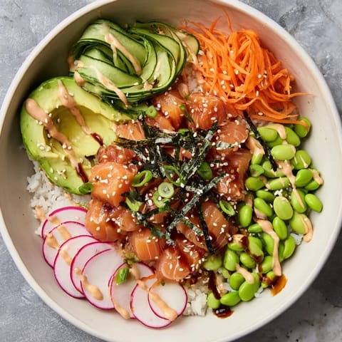 Bright poke bowl with marinated salmon, edamame, and shredded carrots, drizzled with spicy mayo and sesame seeds for a flavorful finish.