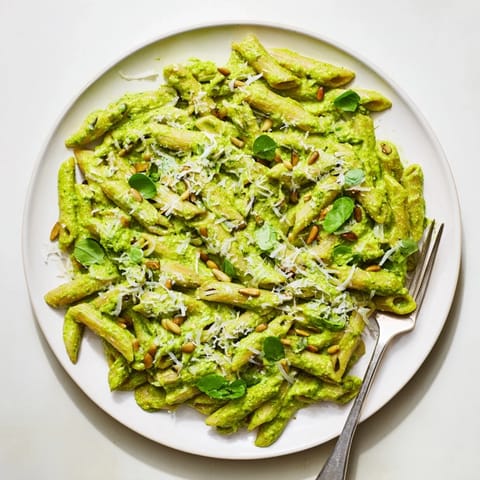 A close-up of Creamy Sunflower Seed Pesto Pasta, topped with grated Parmesan and fresh basil leaves.  