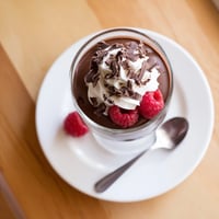 Creamy chocolate pudding in a glass topped with chocolate shavings and fresh raspberries.