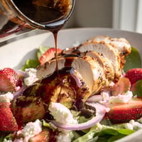 Freshly grilled honey balsamic chicken slices rest atop a vibrant bed of mixed greens, dotted with sliced strawberries, crumbled goat cheese, and toasted pecans for a perfect lunch salad.