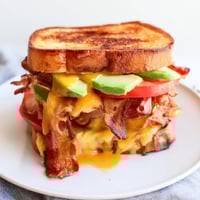 A close-up of the Avocado BLT Grilled Cheese showing melted cheese oozing from the golden, crispy sourdough bread.