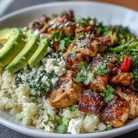 Golden-brown chicken and tender cauliflower rice bowl topped with avocado, cherry tomatoes, and fresh cilantro.